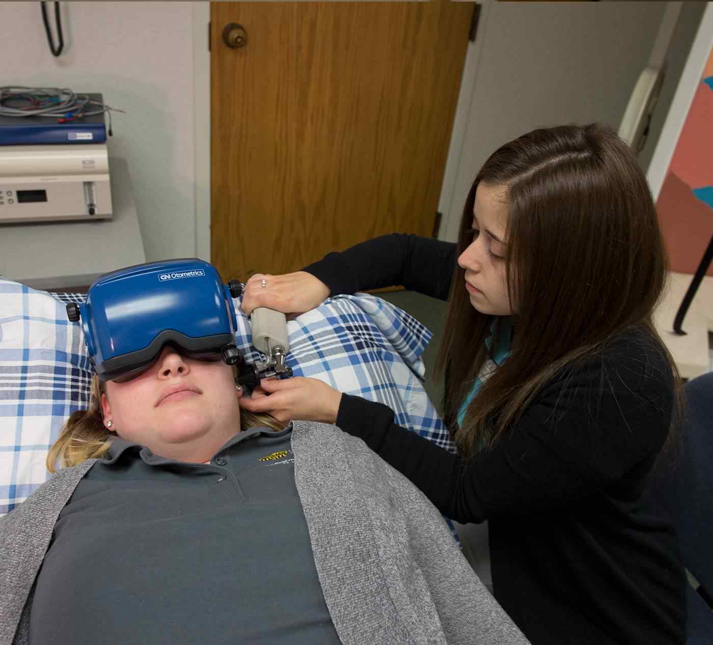 Communications Science and Disorders student applying a headset over a subject's eyes. 